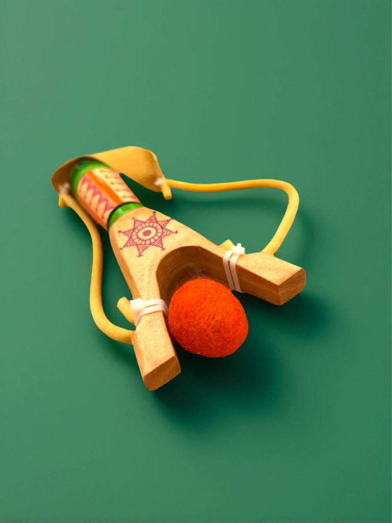 Wooden slingshot with an orange ball on a green background