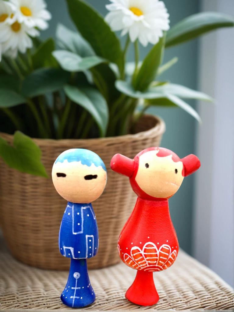 Two colorful wooden dolls, one blue and one red, with a plant in the background.