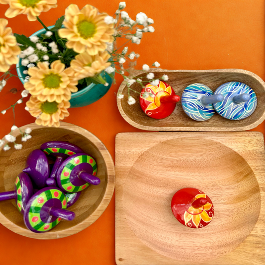 Colorful wooden tops on a wooden surface with an orange background